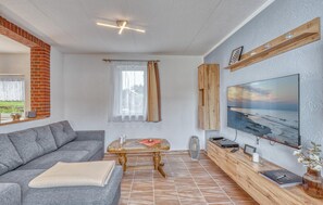 Un salon moderne avec un canapé gris, une table basse en bois, un téléviseur fixé au mur et une cheminée en briques.