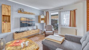 Ein Wohnzimmer mit Fernseher, Holzmöbeln, einer Couch und einem Essbereich mit Tisch und Stühlen.