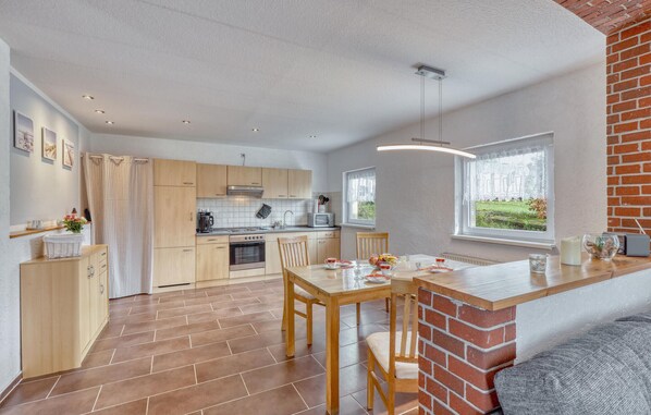 A modern kitchen with wooden cabinets, a dining area with a brick accent wall, and a view of greenery through the window.