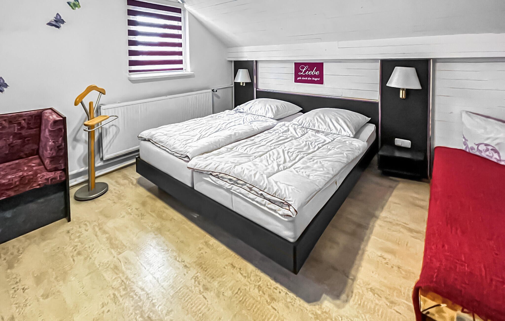 A bedroom with a bed, a nightstand, a lamp, a chair, and a window with blinds.