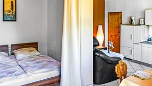 A bedroom with two beds, a dining area with a table and chairs, and a kitchen with cabinets and a refrigerator.
