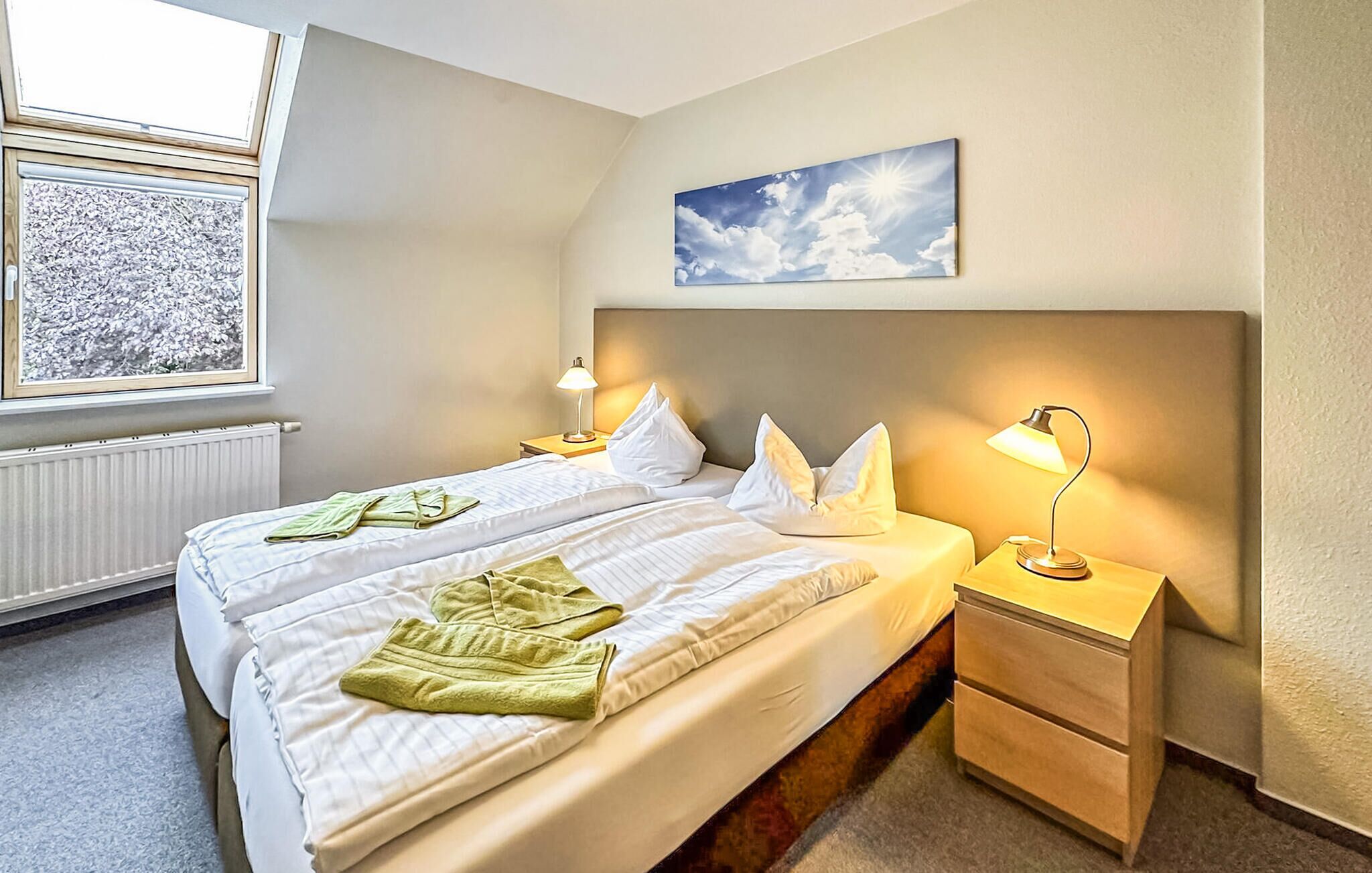 Ett hotellrum med en säng, två sängbord, ett fönster med utsikt över träd och en tavla på väggen.