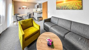 En moderne stue med en gul lænestol, en grå sofa og et træsofabord med blomsterarrangement.