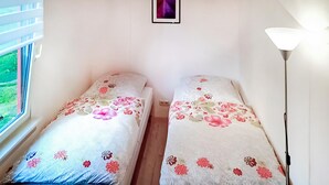 Een kleine kamer met twee bedden, elk met bloemenbedrukking. Links een raam en rechts een vloerlamp.