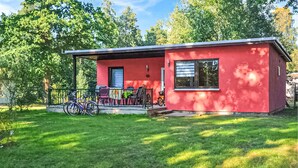 Een rode eenlaags woning met een veranda, fietsen en een gazon.