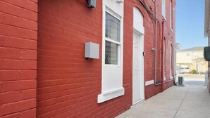 A red brick building with a white door and window, a small white mailbox, and a concrete sidewalk.