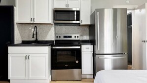 A compact kitchen with white cabinets, a microwave, a stove, and a refrigerator.