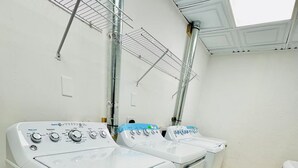 A laundry room with two front-loading washing machines, a metal drying rack, and a skylight above.