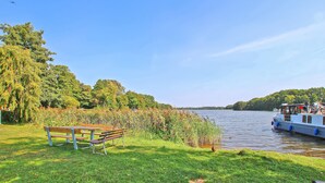 A riverside bench with a view of a boat and trees. - Ferienwohnung Kleinzerlang (Rheinsberg OT Kleinzer)