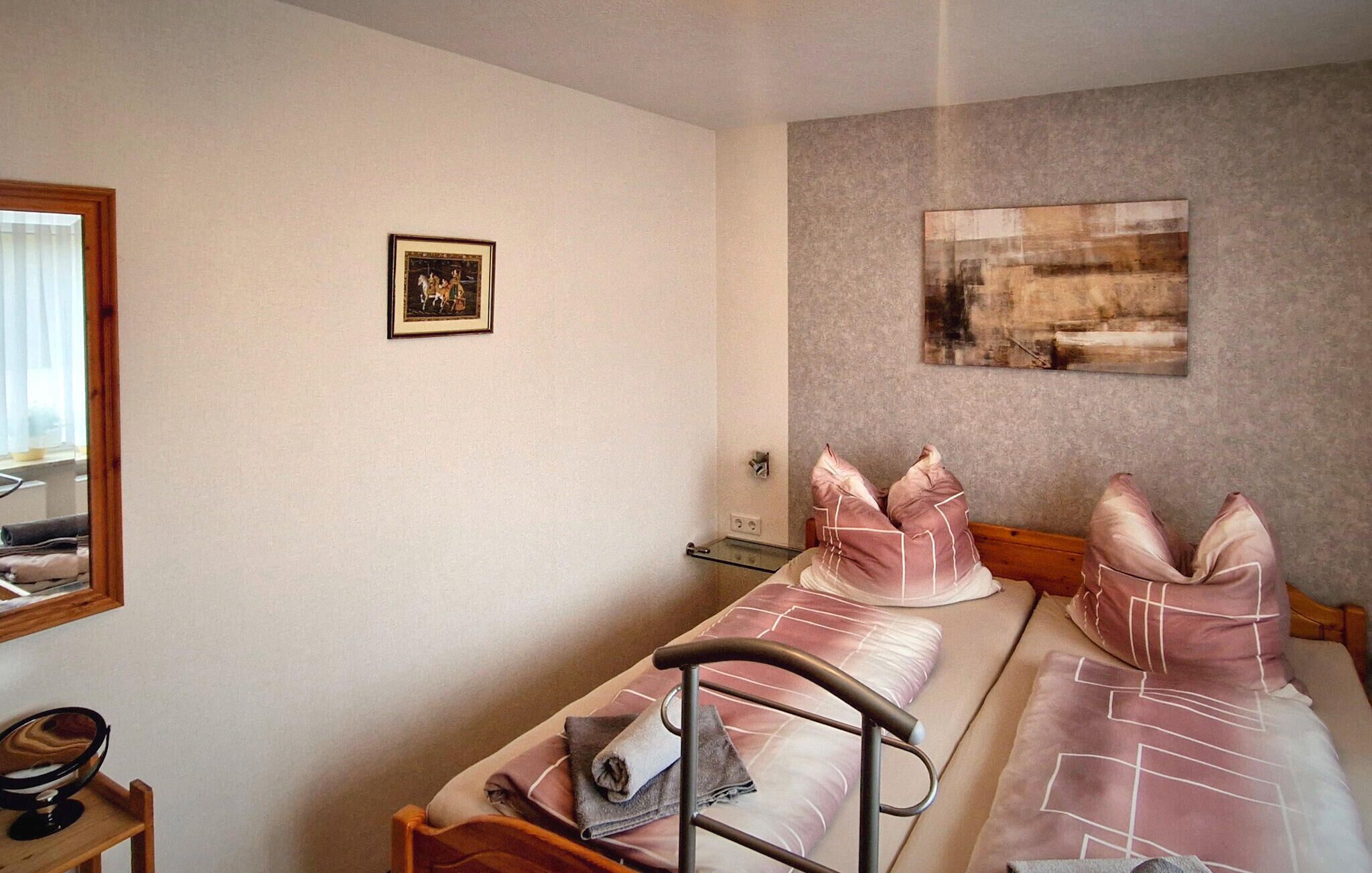 Ein Schlafzimmer mit zwei Betten, einem Nachttisch, einem Spiegel, einem gerahmten Bild an der Wand und einem Gemälde über den Betten.