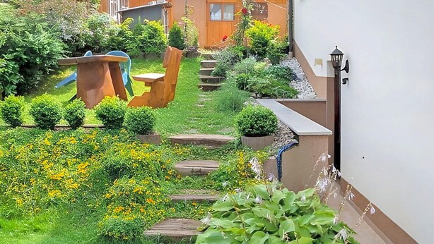 A garden with a wooden bench, a small table, and a pathway leading to a house. - Ferienwohnung Brotterode (Brotterode-Trusetal)
