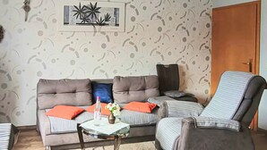 A living room with a sofa, armchair, and a small table with a vase and a bottle. - Ferienwohnung Brotterode (Brotterode-Trusetal)
