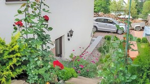 A white building with a garden in front, a parked car, and a white van in the background. - Ferienwohnung Brotterode (Brotterode-Trusetal)