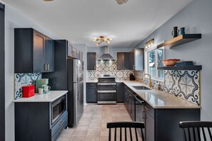 Une cuisine moderne avec des meubles de couleur sombre, un réfrigérateur en acier inoxydable, un four double et un revêtement mural en carreaux.