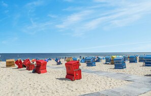 Una playa con filas de sillas y sombrillas rojas y azules, y una vista despejada del océano.