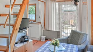 Une petite cuisine équipée avec un téléviseur, une machine à café et un petit placard. Une table recouverte d’une nappe à carreaux et ornée d’un vase de fleurs se trouve au premier plan.
