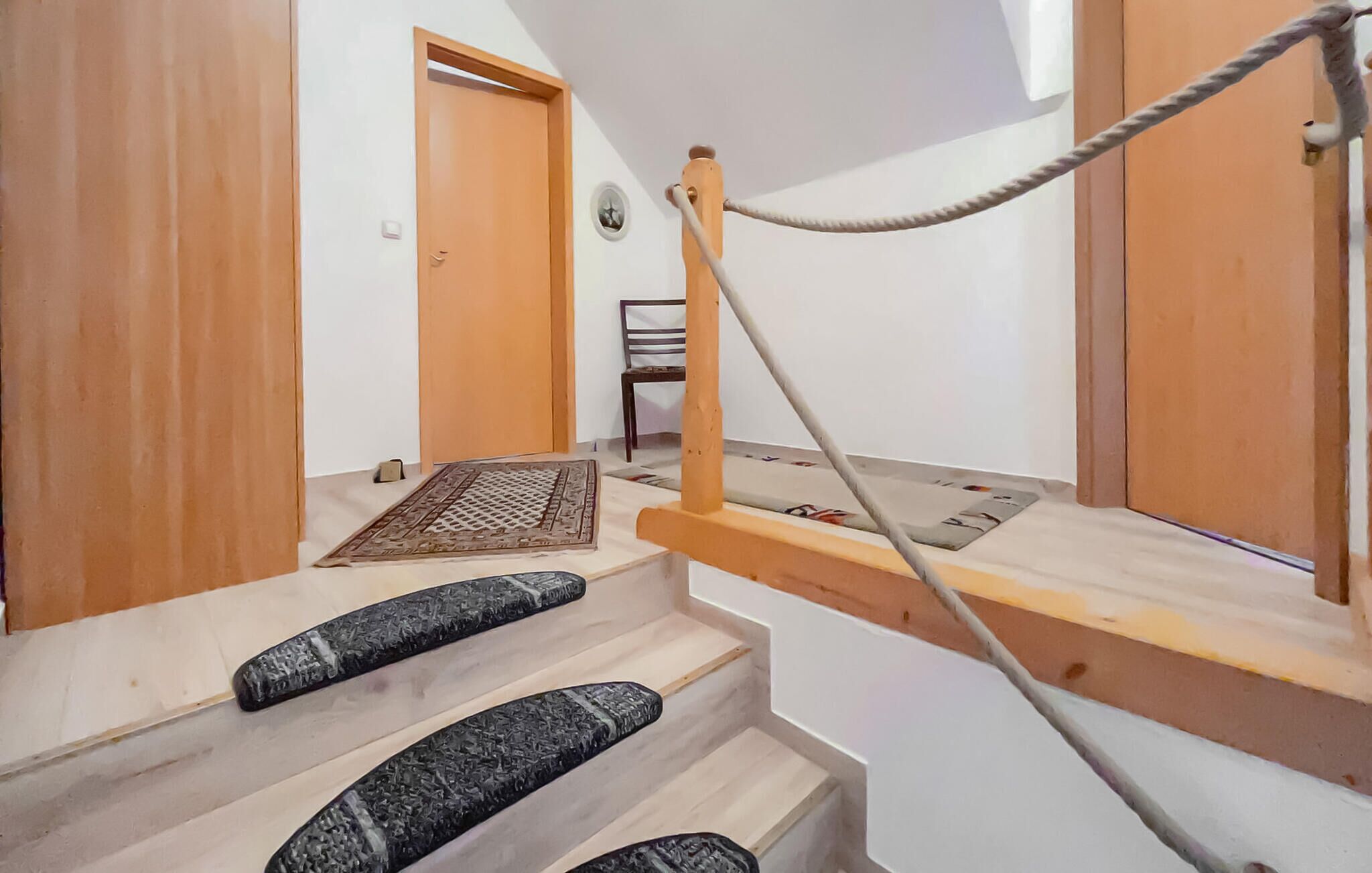 Un escalier avec une échelle de corde, une porte en bois et une chaise à l’arrière-plan.