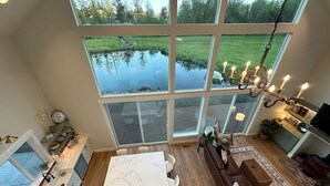 Ett rymligt kök med en stor köksö, en matplats med en brun lädersoffa och utsikt över en damm genom stora fönster.