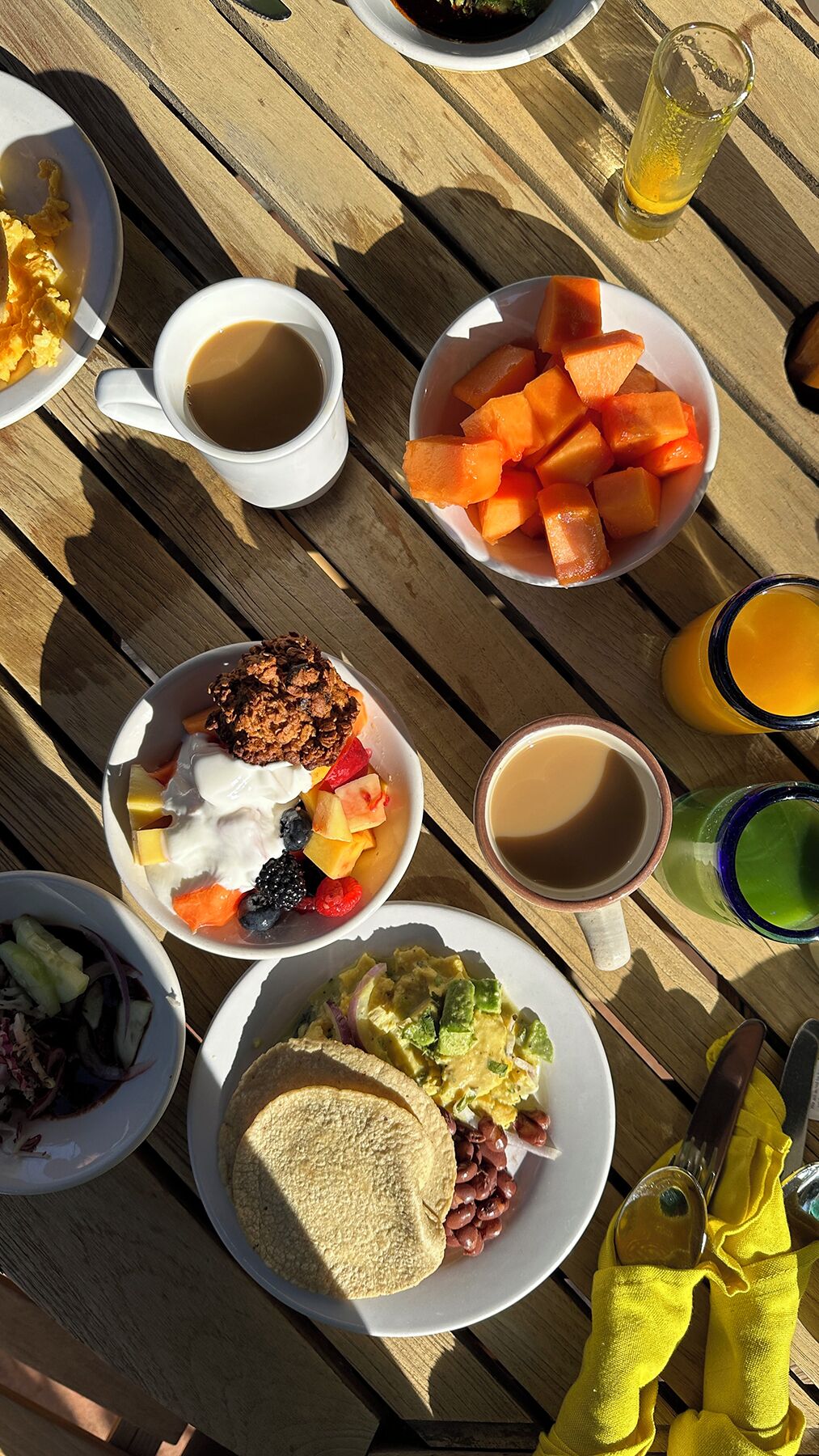 A wooden table with various breakfast items including toast, beans, salad, fruit, and beverages.