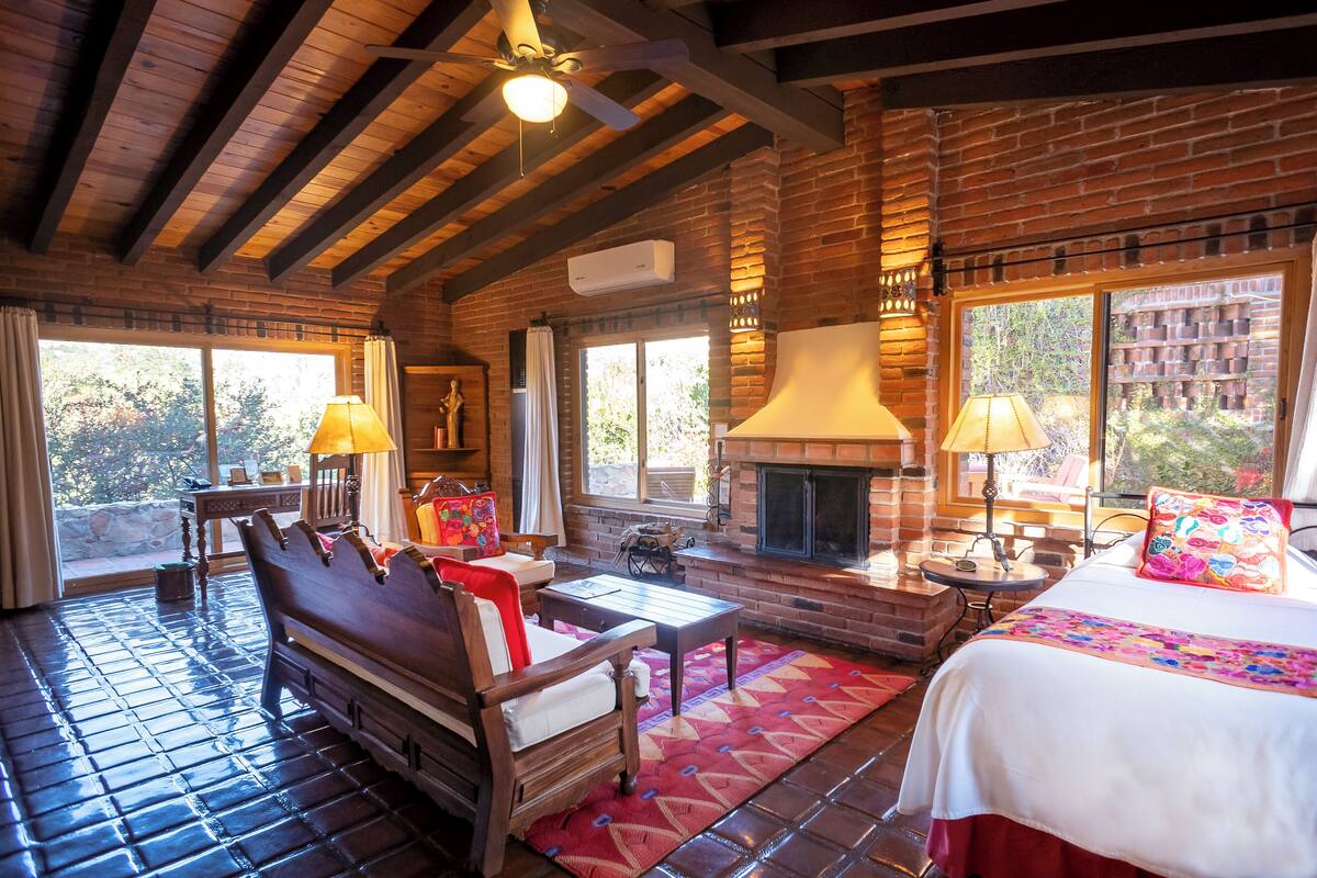 A rustic room with a fireplace, wooden furniture, and large windows.