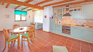 Une cuisine équipée d’une cuisinière, d’un four et d’un évier. On y trouve une table à manger avec des chaises et une fenêtre avec des stores.