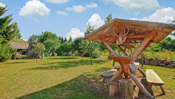 Un cadre extérieur rustique, avec une structure en bois agrémentée d’un crâne de cerf, de tables de pique-nique et d’un mur en pierre.