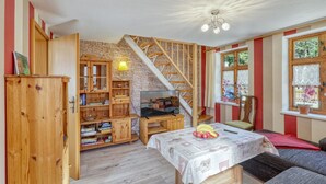 A cozy room with a wooden staircase, a dining table with a tablecloth, and a TV on a wooden stand.