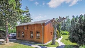 A wooden cabin with a sloped roof, a small porch, and a paved driveway leading to the entrance.