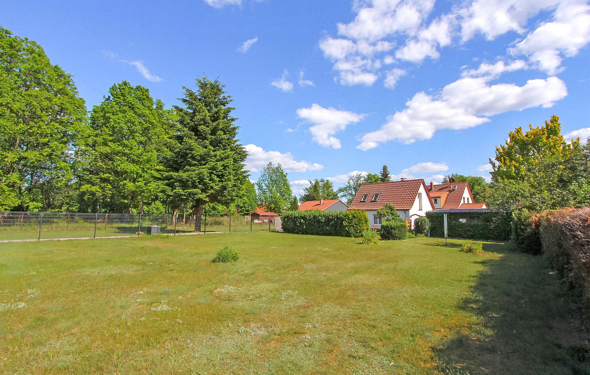 A residential area with a grassy field, trees, and houses with red-tiled roofs.