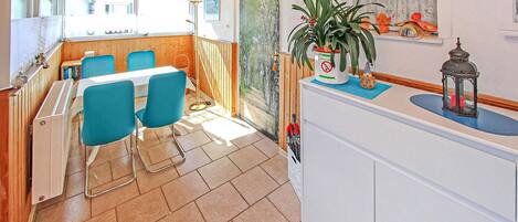 A dining area with a wooden table and blue chairs, a white counter with a plant, and a window with a view of greenery.