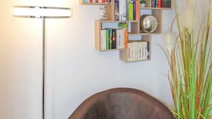 Moderni olohuone, jossa on tummanruskea nojatuoli, lattiavalaisin ja kirjahylly täynnä kirjoja.