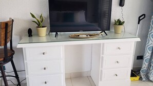 Een wit bureau met een flatscreen televisie, twee planten in potten, een telefoon en een stoel.