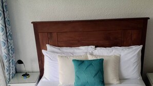 Een net opgemaakt bed met een blauwgroene plaid, witte kussens en een houten hoofdbord.