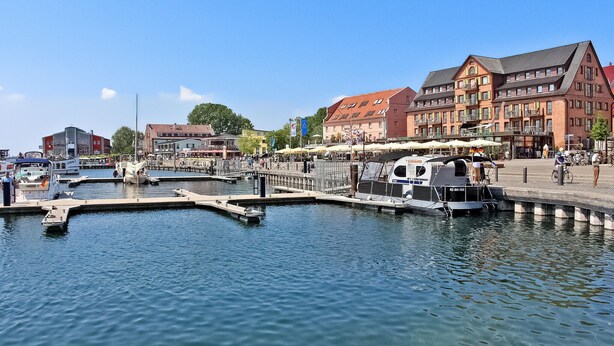 A marina with boats docked, a small boat rental service, and buildings with commercial establishments. - Ferienhaus Waren (Müritz) (Waren (Müritz))