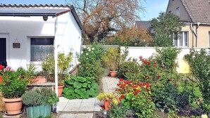 A white house with a tiled roof, surrounded by a garden with various potted plants and flowers. - Ferienhaus Waren (Müritz) (Waren (Müritz))