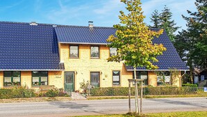 En tvåvåningsbyggnad med ett blått tak täckt av takpannor, en grön dörr och ett litet träd på framsidan av trädgården.