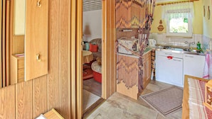 Eine Holztür führt in eine Küche mit Spüle, Wasserkocher und einem Fenster mit Vorhängen.