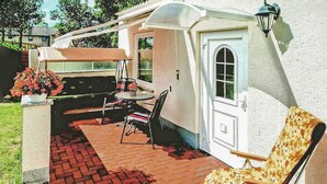 Eine Terrasse mit Tisch und Stühlen, ein überdachter Sitzbereich und eine Tür mit Fenster.