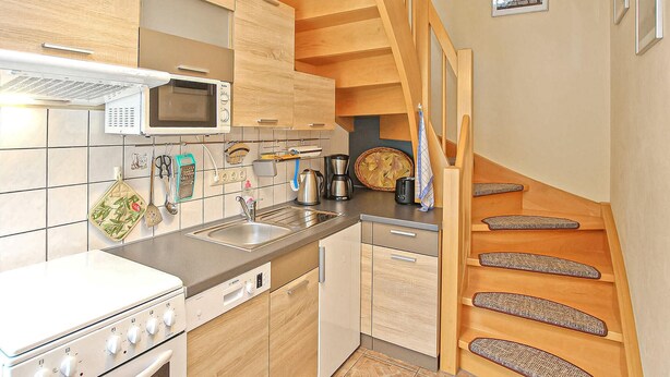 A modern kitchen with wooden cabinets, a stainless steel sink, a Bosch dishwasher, and a microwave. There is a staircase with wooden steps and a basket on the landing. - Cozy apartment in Waren (Müritz) (Waren (Müritz))