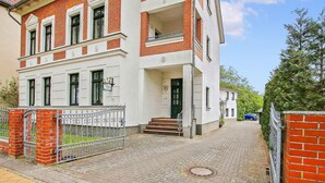 A two-story building with a white facade and red brick accents, featuring a gated entrance and a visible staircase leading to the entrance. - Cozy apartment in Waren (Müritz) (Waren (Müritz))