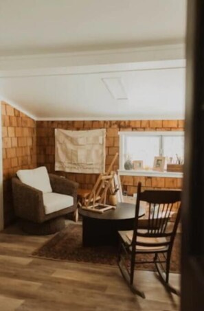 Relax in a cozy room with a brick wall backdrop, featuring a comfortable armchair and a small dining area with a wooden rocking chair.