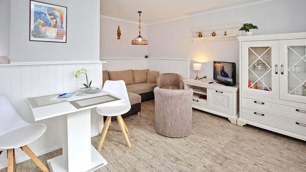 Ein modernes Wohnzimmer mit einem weißen Sofa, einem Esstisch und einem Fernseher auf einem Schrank.