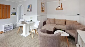 Ein modernes Wohnzimmer mit einem weißen Esstisch, zwei weißen Stühlen, einem braunen Sofa und einem kleinen weißen Beistelltisch.