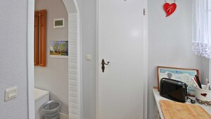 Ein schmaler Flur mit einer weißen Tür, einem Holzschrank, einem Wäschekorb und einem Toaster auf einem Holztisch.