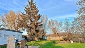 Ein Wohnhaus mit Terrasse, einer Holzterrasse und einem großen Nadelbaum.