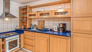 A kitchen with wooden cabinets, a stove, a sink, and a coffee maker. - Ferienwohnung Walow Strietfeld (Walow OT Strietfeld)