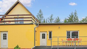 A yellow building with a triangular roof, a white door, and a window. There is a table with chairs outside. - Ferienwohnung Walow Strietfeld (Walow OT Strietfeld)