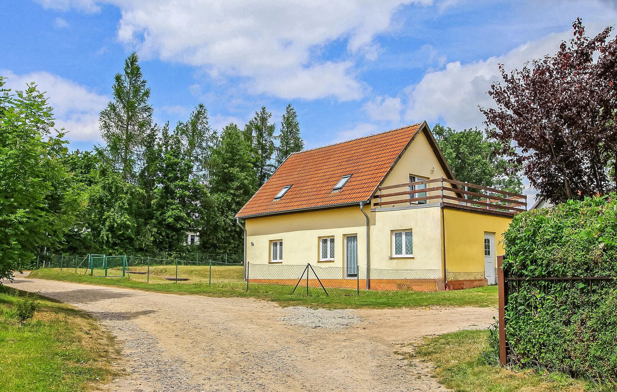 A single-story yellow house with a red-tiled roof, a fenced yard, and a gravel path leading to the entrance.