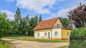 A single-story yellow house with a red-tiled roof, a fenced yard, and a gravel path leading to the entrance. - Ferienwohnung Walow Strietfeld (Walow OT Strietfeld)