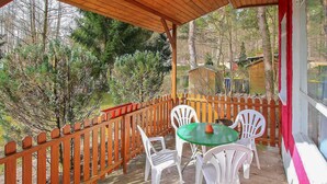 A covered outdoor patio with a table and chairs, surrounded by a wooden fence and trees.